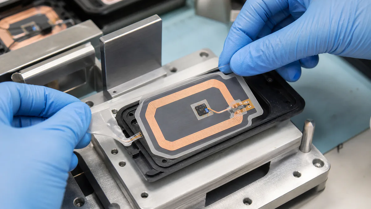 Gloved electronics technician aligning a custom die-cut adhesive around a copper RFID antenna inlay in an assembly fixture